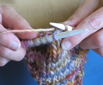 hands holding knitting needles with multi-colored yarn