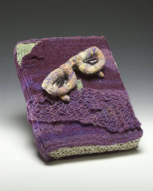 Uncover, fiberart sculpture, purple knitted yarn book with pages knit from paper ribbon, knitted multi-colored eyeglasses, 3 x 7 x 10 in © 2005 Eve Jacobs-Carnahan, Photo by Paul Rogers, Stowe, VT