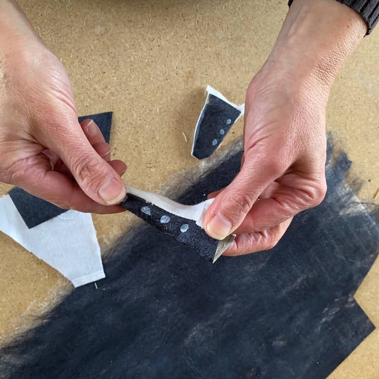 hands holding cone shaped wedge white underside sewn to black silk paper with silk fusion on workbench