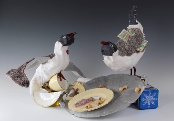 mixed media sculpture of gulls standing over broken china, money, and remains of lunch