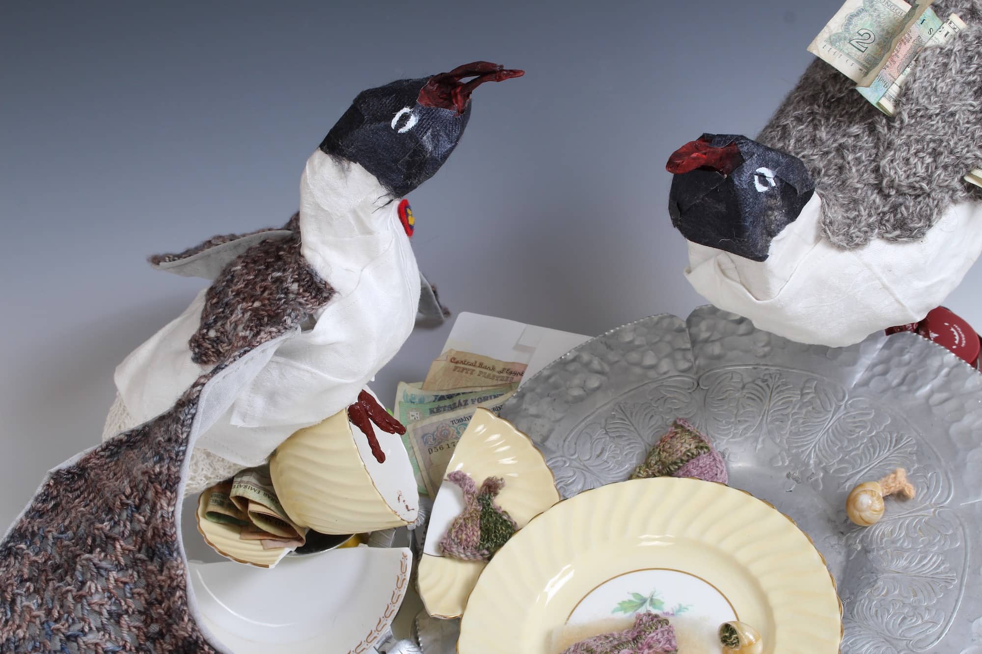 mixed media sculpture of gulls standing over broken china, money, and remains of lunch