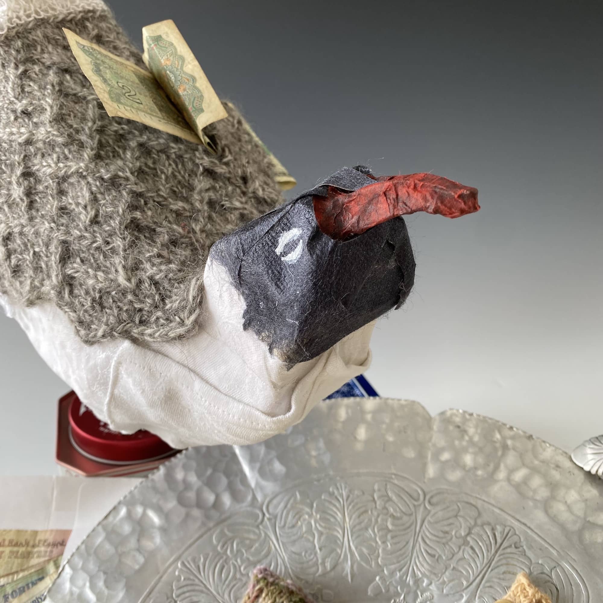 mixed media sculpture of gull perched on edge of metal platter with money tucked under wing