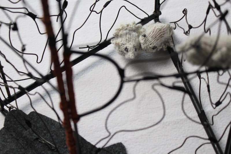 detail of knitted grey birds cowering in corner of wire cage-sculpture by Eve Jacobs-Carnahan
