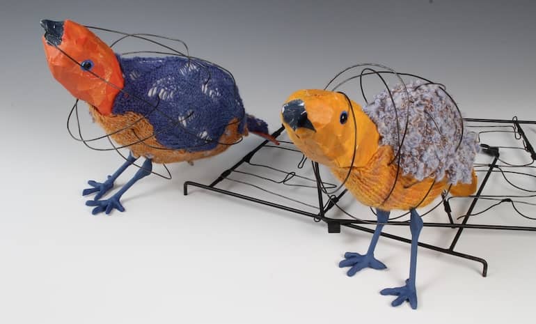 paper, fabric, knitting, and wire sculpture of two birds walking away from broken cage while bodies surrounded with black wire