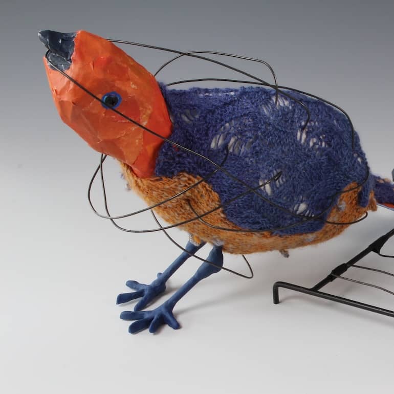 close up of deep yellow orange bird with dark blue violet knitted back and feet with swirling black wire around body and head