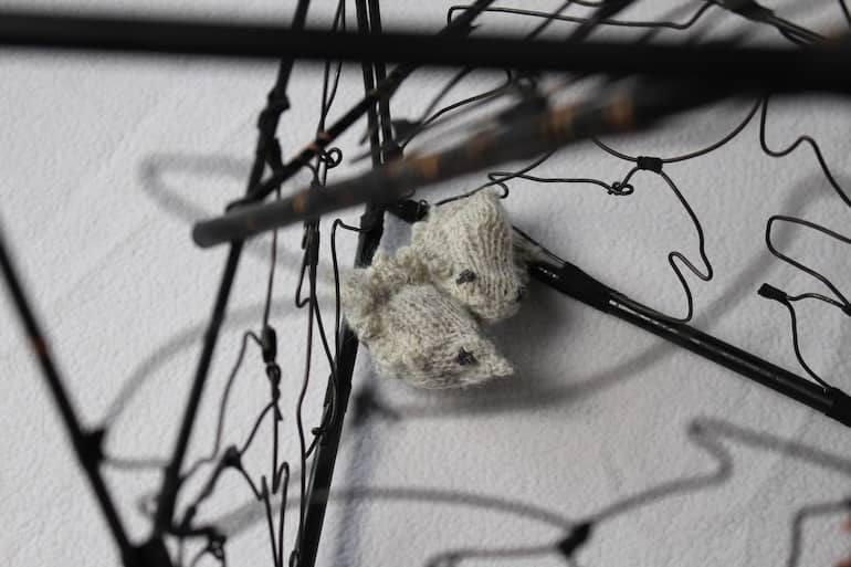 focus detail on two tiny grey knitted birds with black eyes, wire lines of enclosure blurred