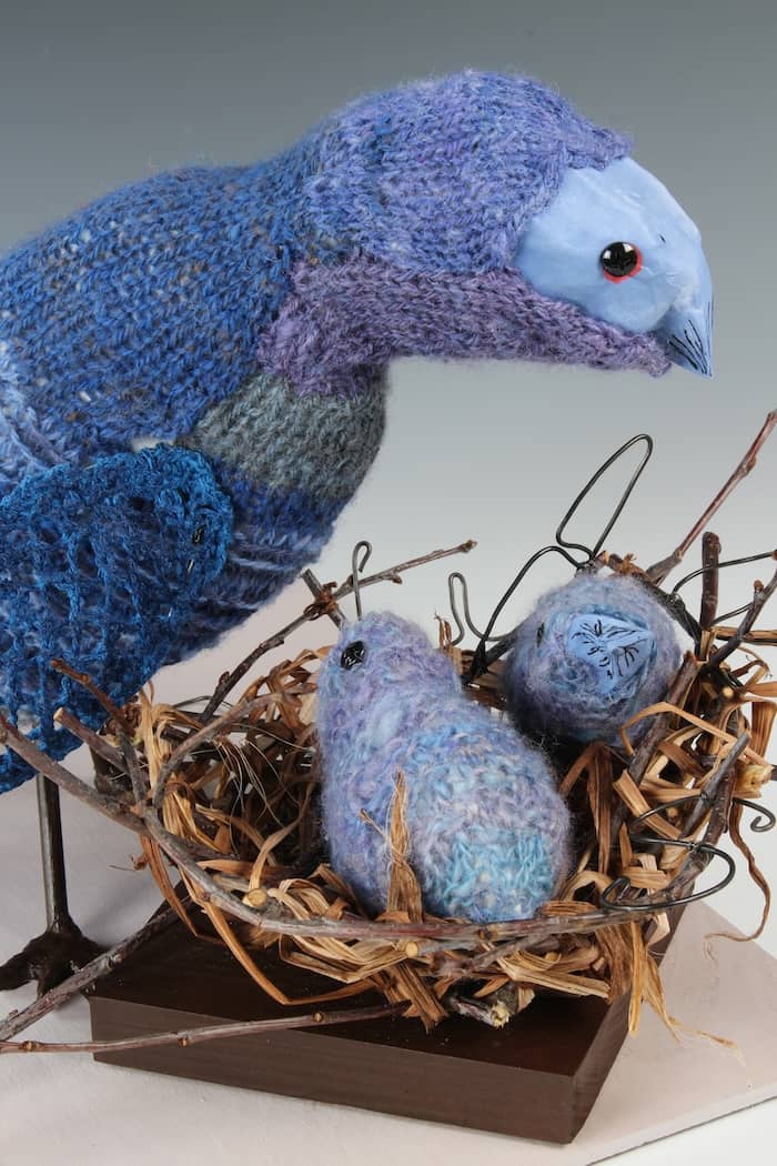 blue knitted bird standing guard over chicks in nest